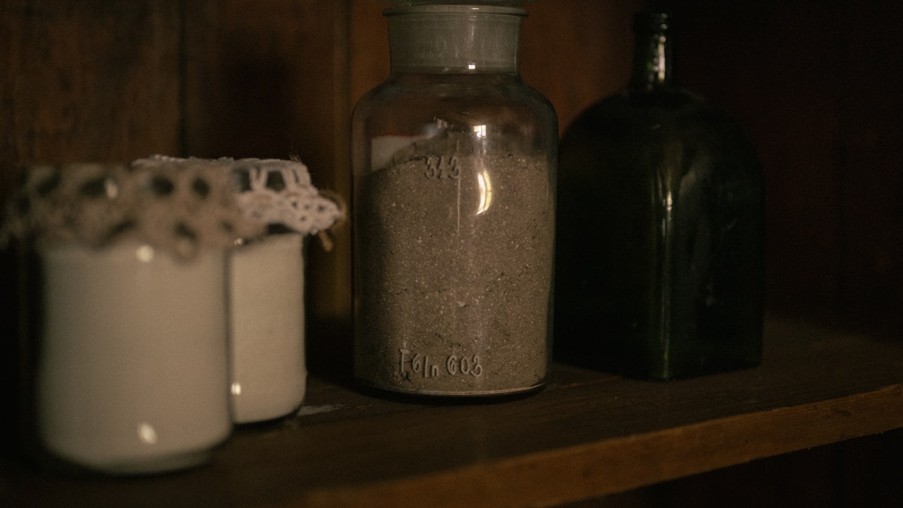 Old glass jars and bottles lined up along a dark wooden shelf behind a merchant's counter