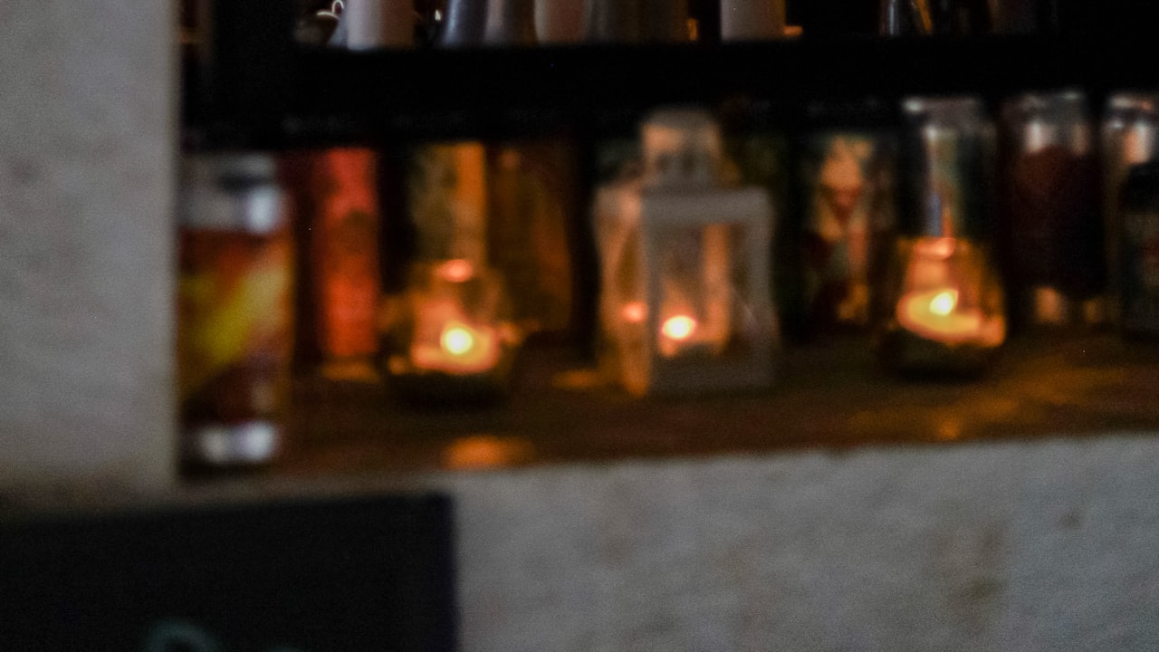 A bartender seen through a window, preparing drinks beside shelves of bottles and lit candles
