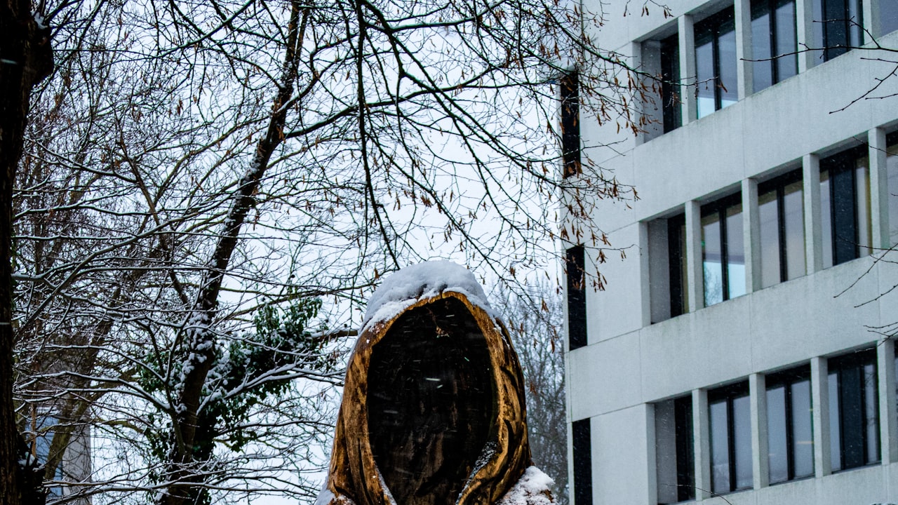A hooded, cloaked figure holding a lantern aloft in falling snow